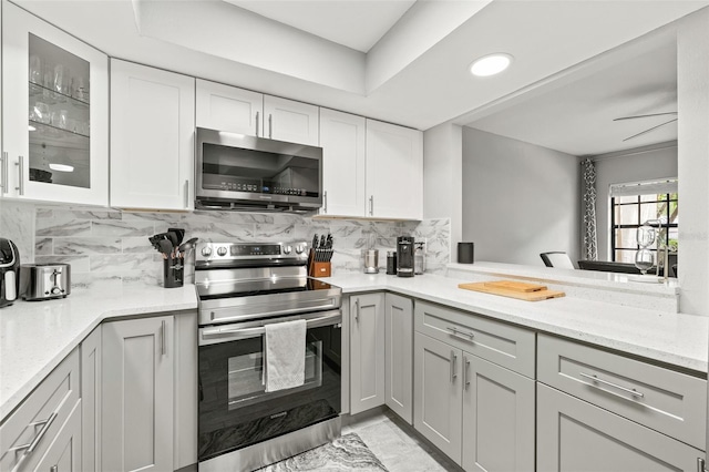 kitchen with light stone counters, backsplash, stainless steel appliances, and kitchen peninsula