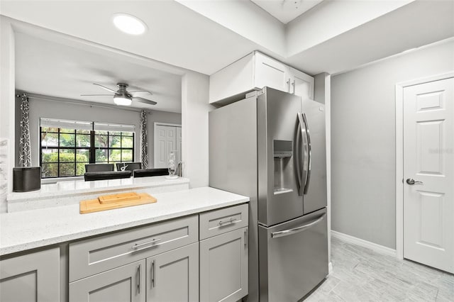 kitchen with light stone counters, ceiling fan, stainless steel fridge with ice dispenser, and gray cabinetry