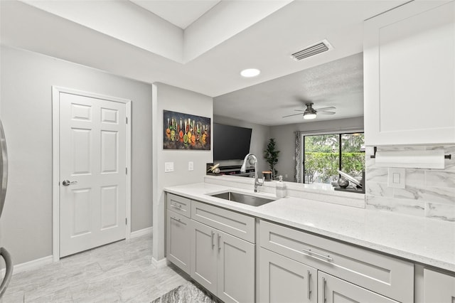 kitchen with sink, ceiling fan, backsplash, light stone counters, and kitchen peninsula