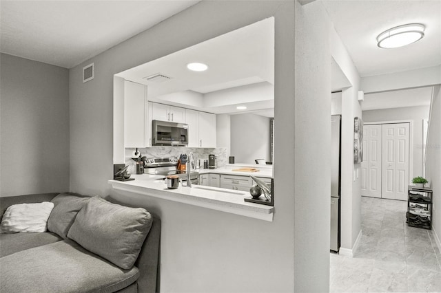 kitchen featuring white cabinetry, stainless steel appliances, kitchen peninsula, and decorative backsplash