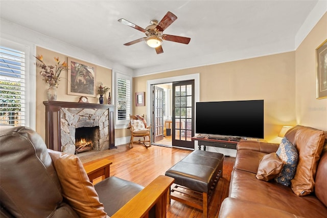 living room with a stone fireplace, hardwood / wood-style floors, and ceiling fan