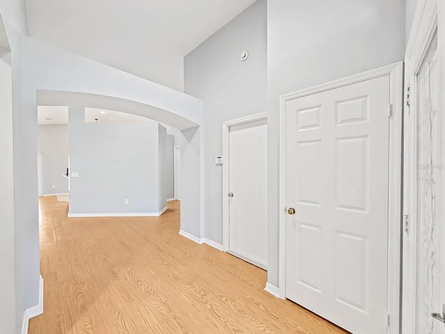 unfurnished room with light wood finished floors, baseboards, arched walkways, and high vaulted ceiling