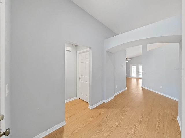 hall featuring lofted ceiling, light wood finished floors, baseboards, and french doors