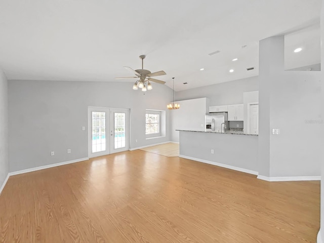 unfurnished living room with light wood-style floors, ceiling fan with notable chandelier, baseboards, and french doors