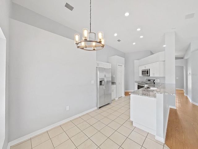 kitchen featuring stainless steel appliances, a peninsula, a sink, white cabinets, and pendant lighting