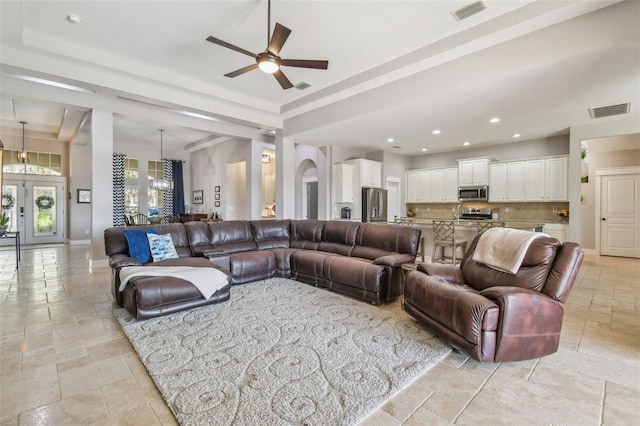 living room featuring stone tile floors, visible vents, a tray ceiling, and french doors