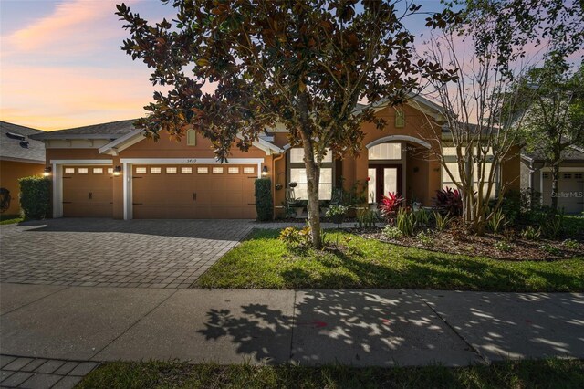 view of front facade featuring an attached garage, stucco siding, decorative driveway, and french doors