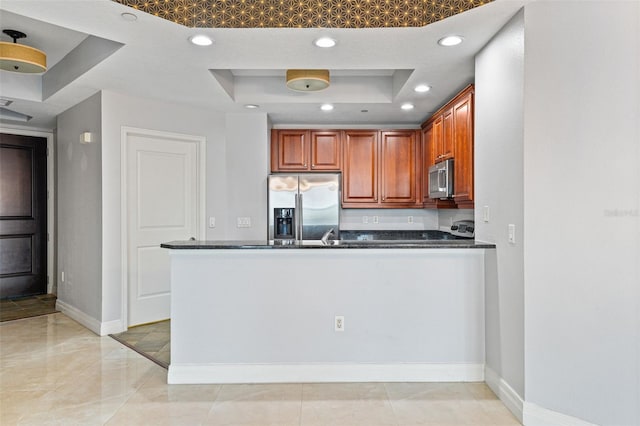 kitchen featuring dark stone countertops, stainless steel appliances, a raised ceiling, and kitchen peninsula