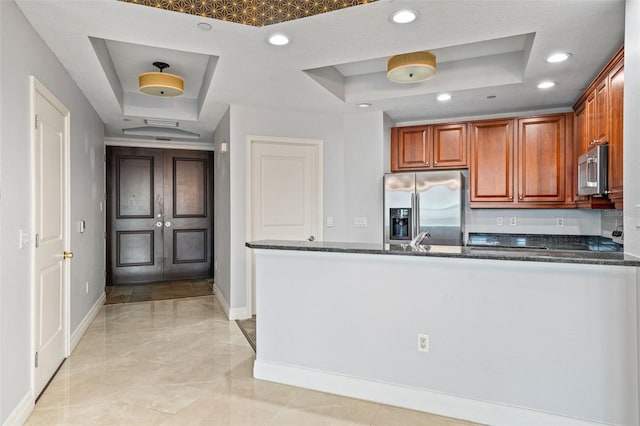 kitchen with stainless steel appliances, a raised ceiling, kitchen peninsula, and dark stone counters
