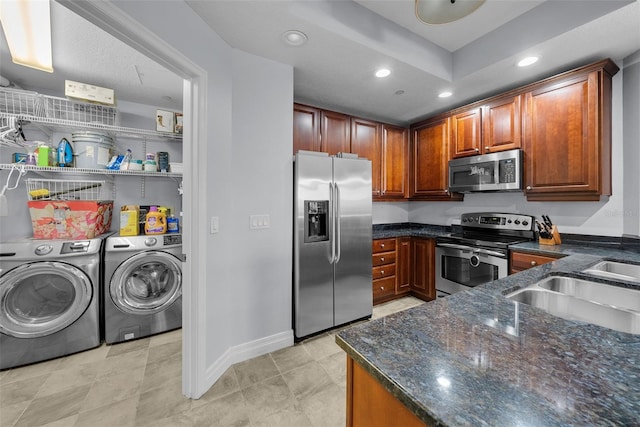 kitchen featuring stainless steel appliances, sink, washing machine and clothes dryer, and dark stone counters