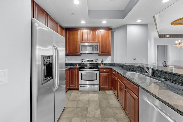 kitchen with stainless steel appliances, sink, dark stone countertops, and a tray ceiling