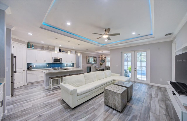 living room with a raised ceiling, ornamental molding, and light wood-type flooring