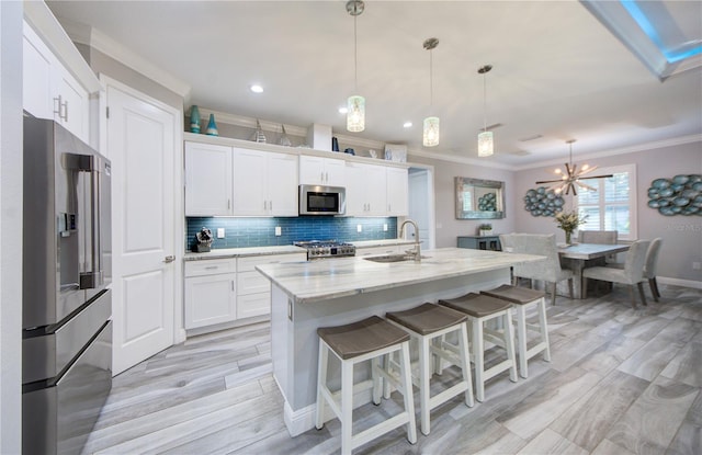 kitchen featuring sink, white cabinetry, appliances with stainless steel finishes, an island with sink, and pendant lighting