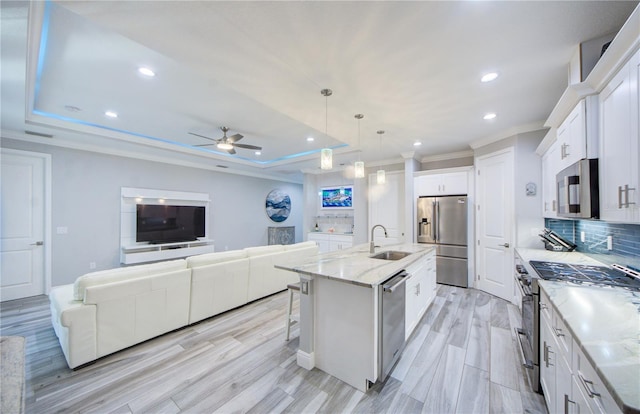 kitchen featuring a center island with sink, appliances with stainless steel finishes, a raised ceiling, pendant lighting, and white cabinets