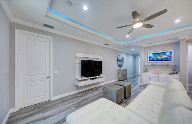 living area featuring a raised ceiling, visible vents, and crown molding