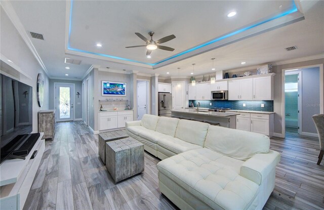 living room with a tray ceiling, light wood-style flooring, visible vents, and crown molding