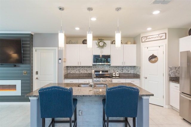 kitchen with appliances with stainless steel finishes, decorative light fixtures, white cabinetry, an island with sink, and sink