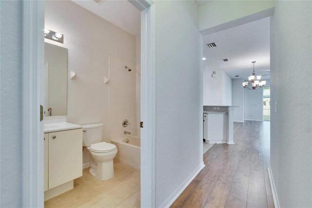 full bathroom featuring wood-type flooring, vanity, toilet, bathing tub / shower combination, and an inviting chandelier