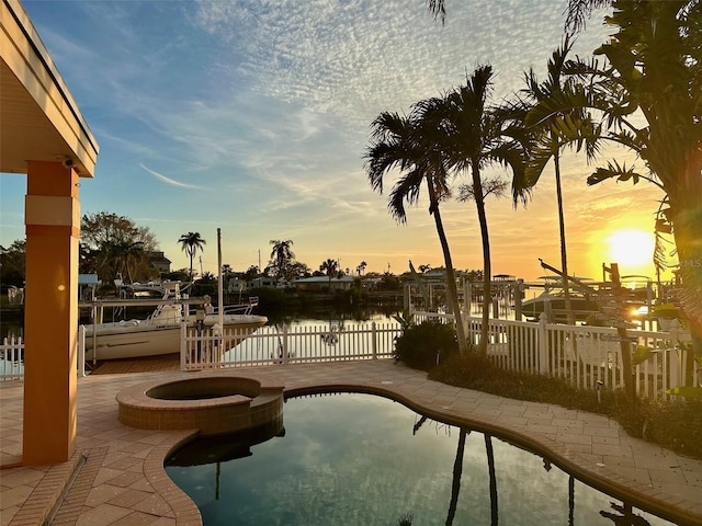 pool at dusk with an outdoor fire pit, a patio area, and a water view