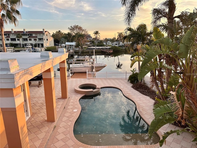 pool at dusk featuring a water view and a patio area