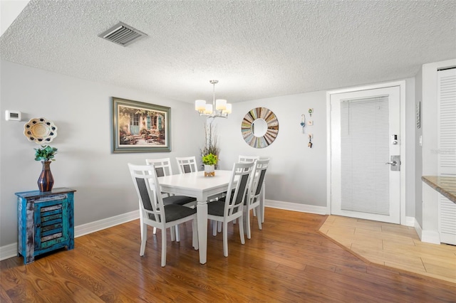 dining area with hardwood / wood-style floors, a textured ceiling, and a chandelier