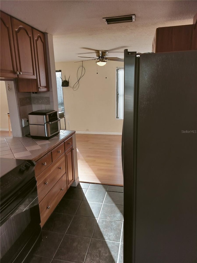 kitchen featuring ceiling fan, black appliances, a textured ceiling, dark tile patterned flooring, and tile countertops