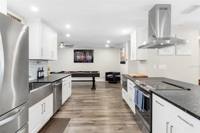 kitchen featuring appliances with stainless steel finishes, island range hood, white cabinets, dark stone counters, and light wood-type flooring