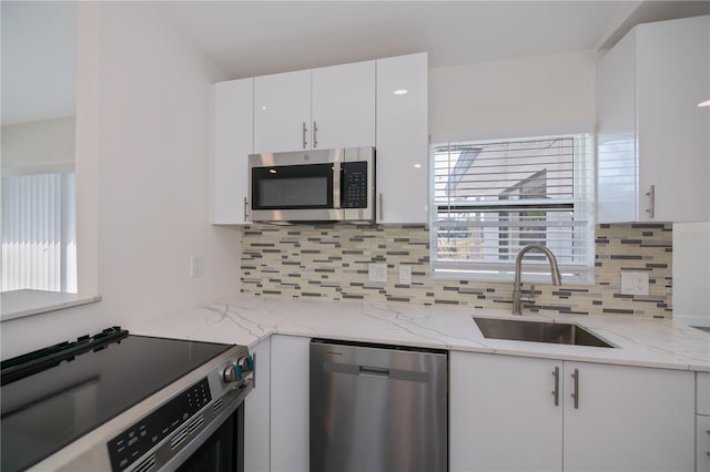 kitchen featuring sink, appliances with stainless steel finishes, white cabinetry, light stone countertops, and decorative backsplash