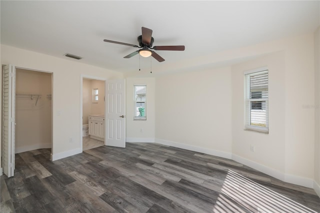 unfurnished bedroom with a walk in closet, ceiling fan, dark wood-type flooring, ensuite bath, and a closet