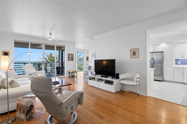 living room with a textured ceiling, ceiling fan, and light wood-type flooring