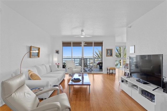 living room with ceiling fan, light hardwood / wood-style flooring, and a textured ceiling