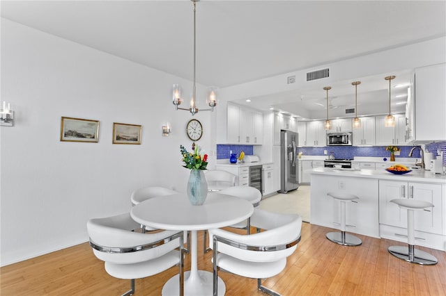 dining area featuring beverage cooler, an inviting chandelier, and light hardwood / wood-style flooring