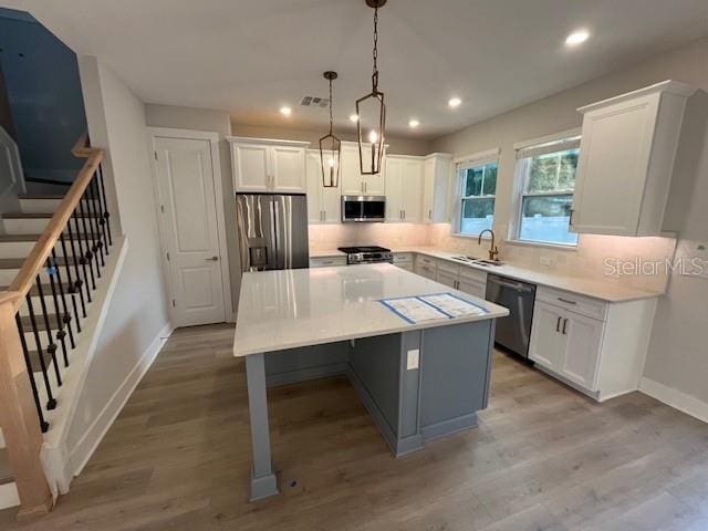 kitchen featuring stainless steel appliances, white cabinetry, a kitchen island, and sink