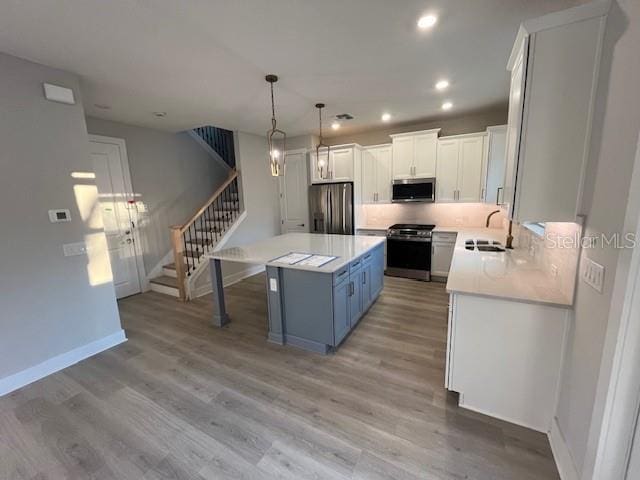 kitchen featuring appliances with stainless steel finishes, blue cabinetry, white cabinets, and decorative light fixtures