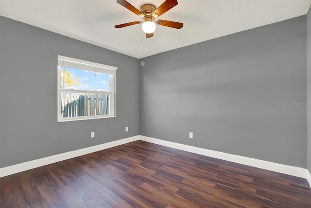 empty room featuring dark wood finished floors, a ceiling fan, and baseboards