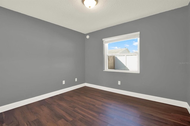 spare room with a textured ceiling, dark wood finished floors, and baseboards