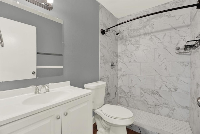 bathroom with toilet, a tile shower, and vanity