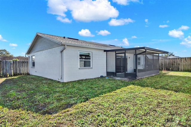 rear view of property with a yard, concrete block siding, a fenced backyard, and a sunroom