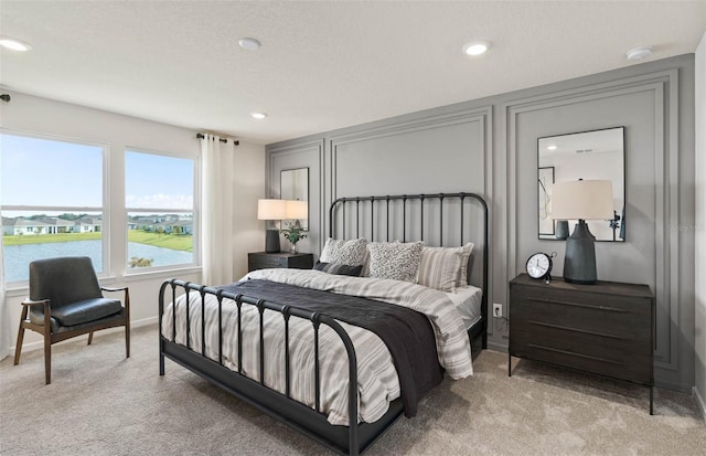 bedroom with a water view, light colored carpet, and a textured ceiling