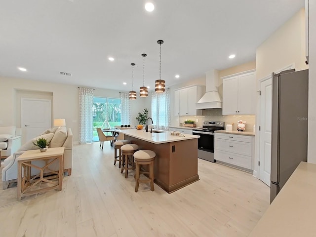 kitchen with premium range hood, white cabinetry, appliances with stainless steel finishes, a center island with sink, and a kitchen bar