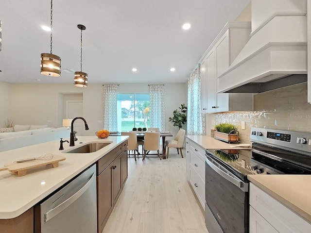 kitchen with appliances with stainless steel finishes, custom range hood, white cabinets, and decorative light fixtures