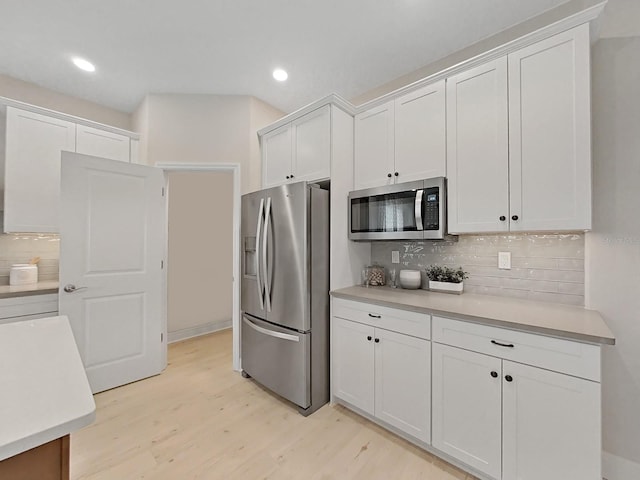 kitchen with white cabinetry, stainless steel appliances, backsplash, and light wood-type flooring