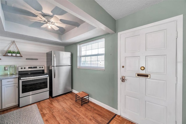 kitchen with stainless steel appliances, a raised ceiling, light countertops, light wood-style floors, and a textured ceiling