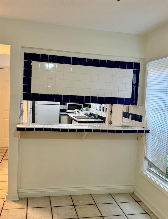 kitchen featuring light tile patterned floors, white refrigerator, tile counters, kitchen peninsula, and decorative backsplash