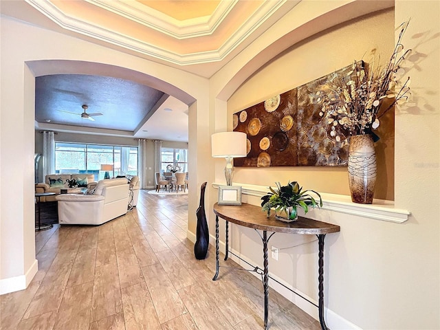 corridor with ornamental molding, arched walkways, a raised ceiling, and baseboards