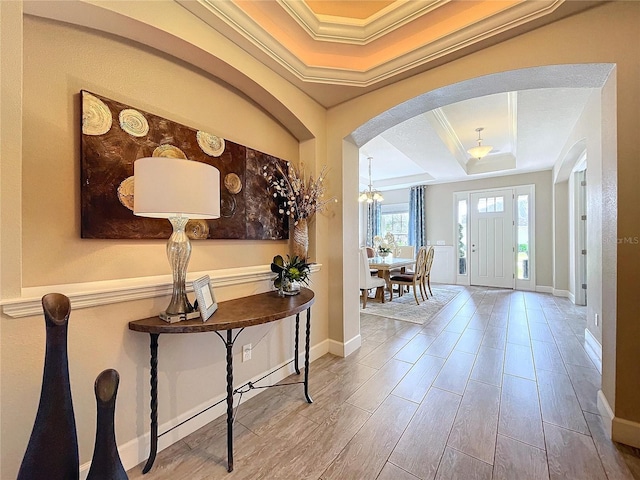 foyer entrance with baseboards, arched walkways, wood finished floors, a tray ceiling, and crown molding