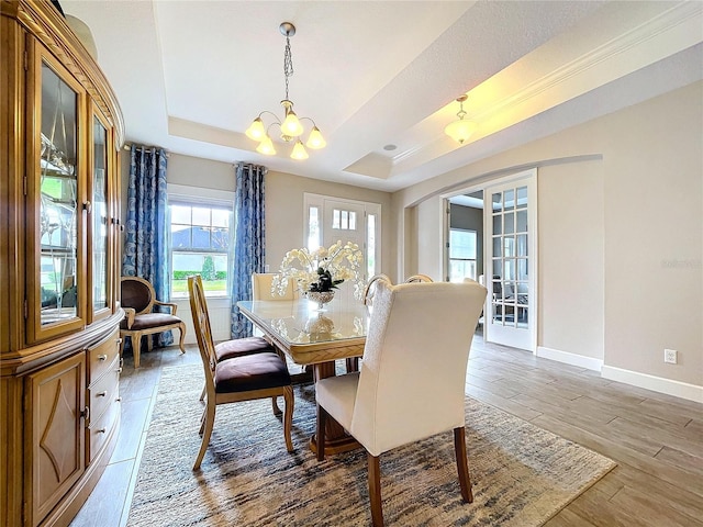 dining area featuring light wood finished floors, baseboards, a raised ceiling, and french doors