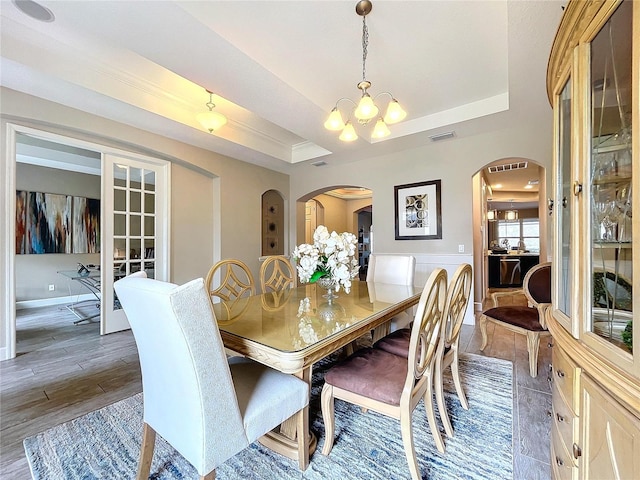 dining room with a tray ceiling, arched walkways, visible vents, an inviting chandelier, and wood finished floors