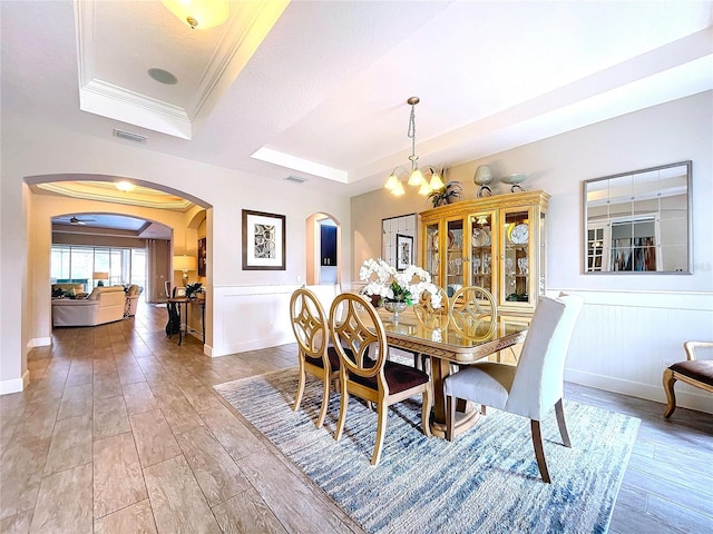 dining space with arched walkways, a wainscoted wall, a raised ceiling, and crown molding