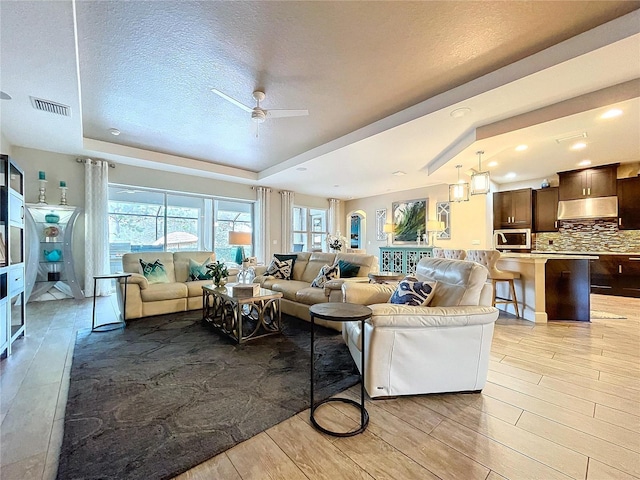 living area with a raised ceiling, visible vents, plenty of natural light, and light wood finished floors